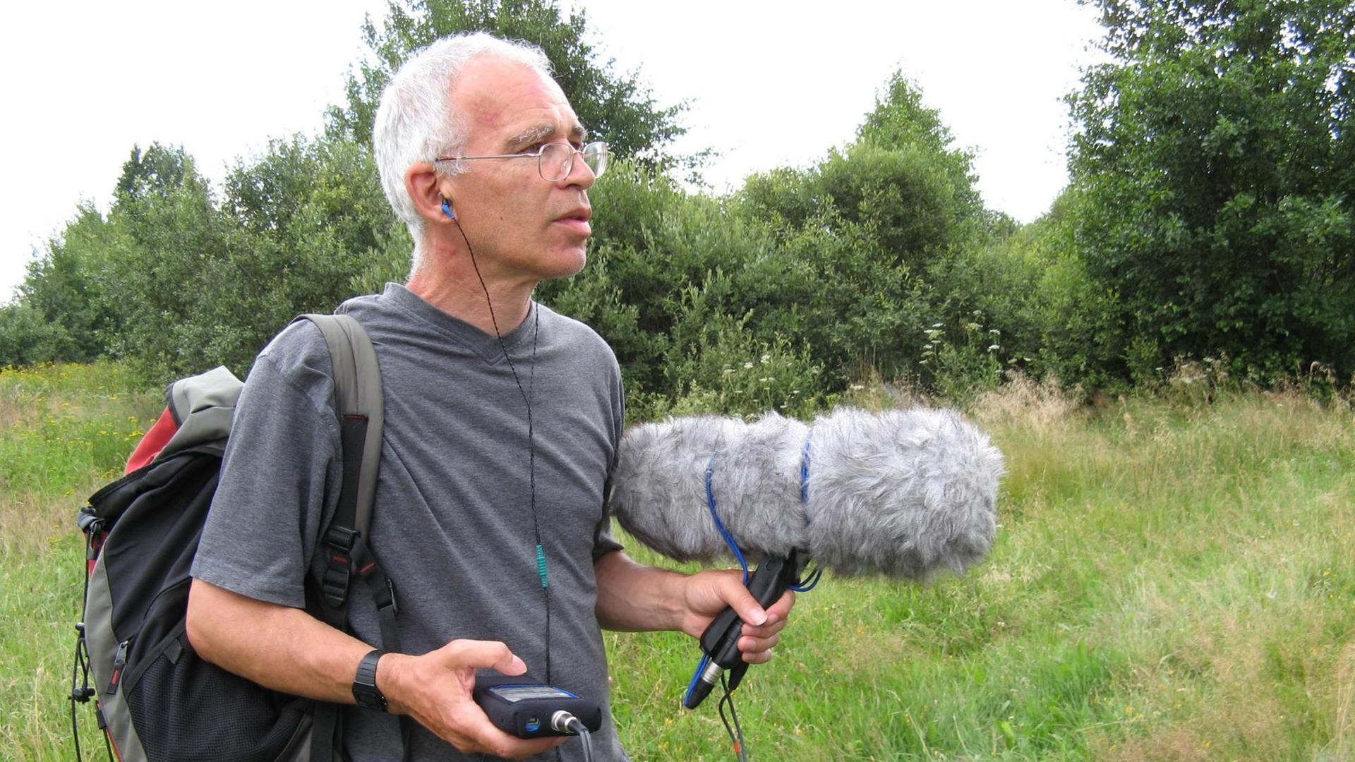 Peter Cusack mit Aufnahmegerät und großem Windschutz bei Feldaufnahmen in offener Landschaft Peter Cusack mit Aufnahmegerät und großem Windschutz bei Feldaufnahmen in offener Landschaft