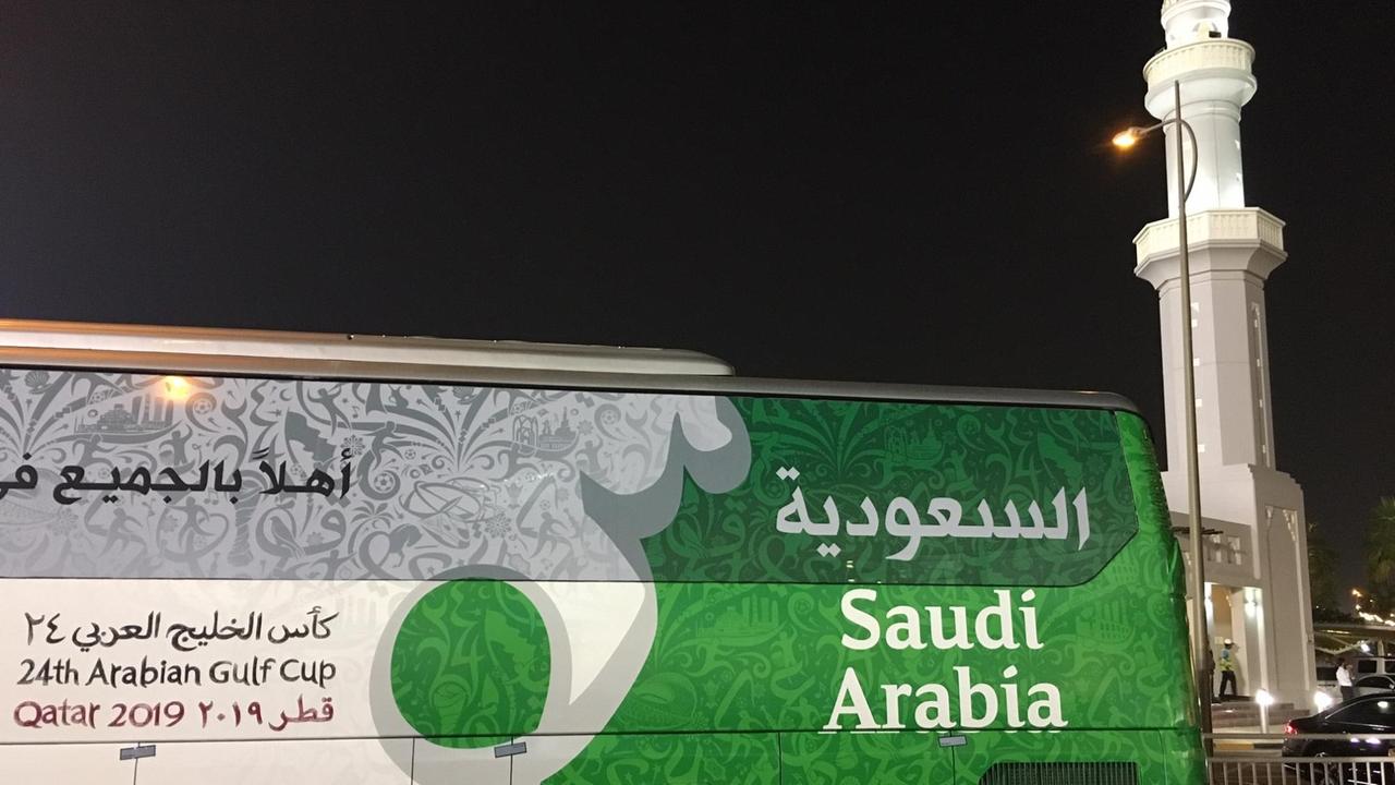Im Vordergrund ein weiß-grüner Bus, auf dem unter anderem "Saudi Arabia" und "24th Arabian Golf Cup Qatar 2019" steht. Im Vordergrund ein weiß-grüner Bus, auf dem unter anderem "Saudi Arabia" und "24th Arabian Golf Cup Qatar 2019" steht.