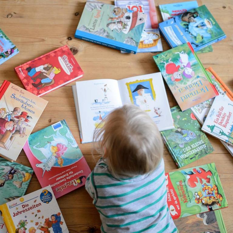ILLUSTRATION: Ein Kind liegt zwischen vielen Büchern und schaut sich ein Buch an, aufgenommen am 28.01.2015 in Dresden (Sachsen). Foto: Thomas Eisenhuth - model released -