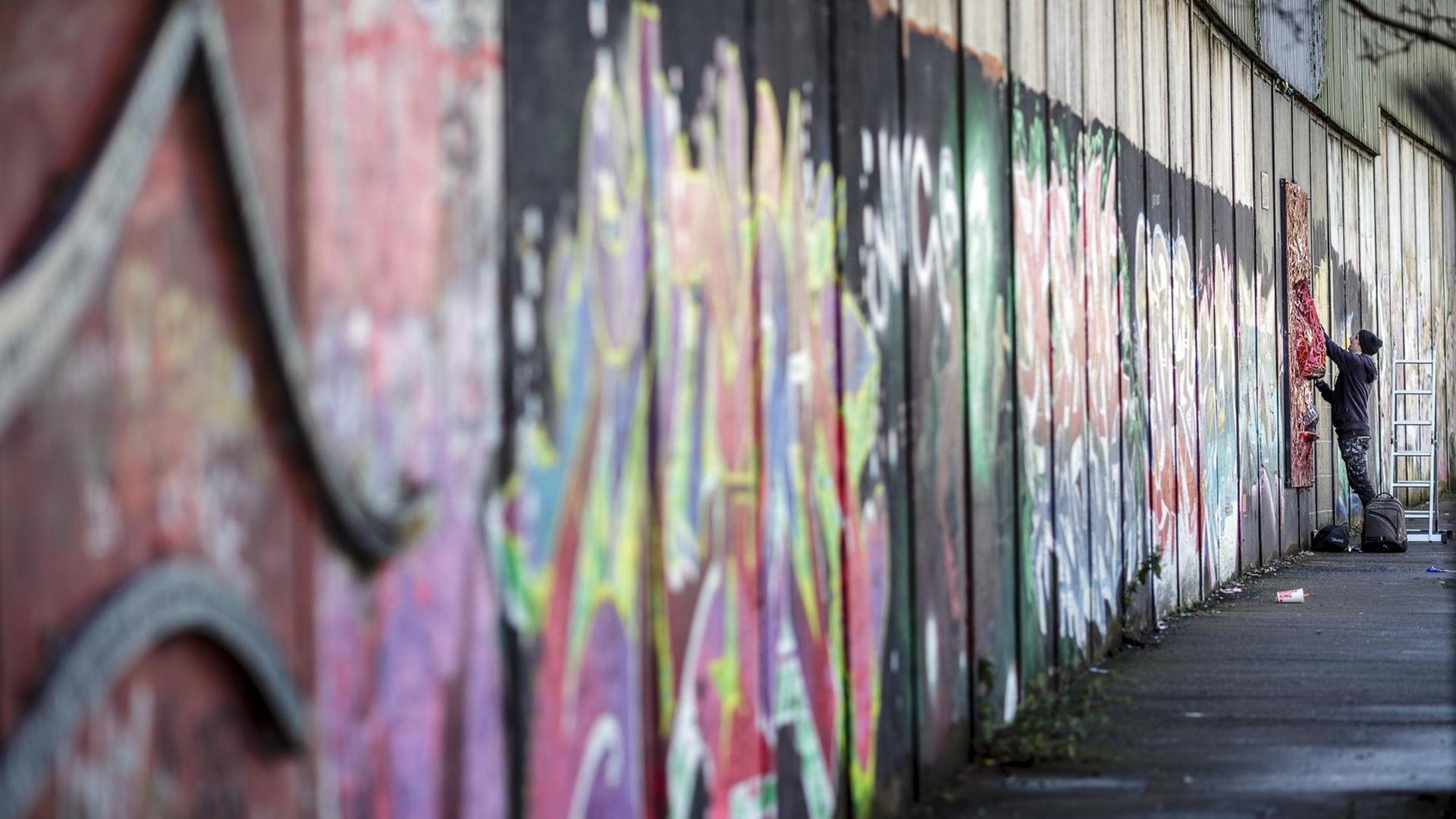 Ein Graffiti-Künstler besprüht am 27.02.2017 in einem pro-britische Teil von Belfast (Nordirland) eine Friedensmauer. Gewaltige Mauern und Metallzäune schlängeln sich durch Belfast, manche über zwölf Meter hoch und gekrönt von Stacheldraht. Sie trennen Wohngebiete voneinander, schnurgerade oder im Zickzack-Kurs. Die Katholiken leben auf der einen Seite, die Protestanten auf der anderen. Ein Graffiti-Künstler besprüht am 27.02.2017 in einem pro-britische Teil von Belfast (Nordirland) eine Friedensmauer. Gewaltige Mauern und Metallzäune schlängeln sich durch Belfast, manche über zwölf Meter hoch und gekrönt von Stacheldraht. Sie trennen Wohngebiete voneinander, schnurgerade oder im Zickzack-Kurs. Die Katholiken leben auf der einen Seite, die Protestanten auf der anderen.