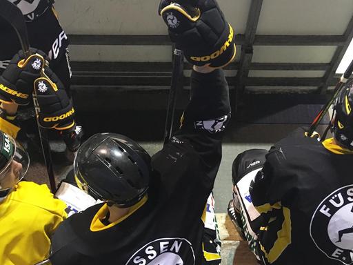 Drei Eishockeyspieler des EV Füssen sitzen, in schwarz gelben Trikots, auf der Spielerbank.