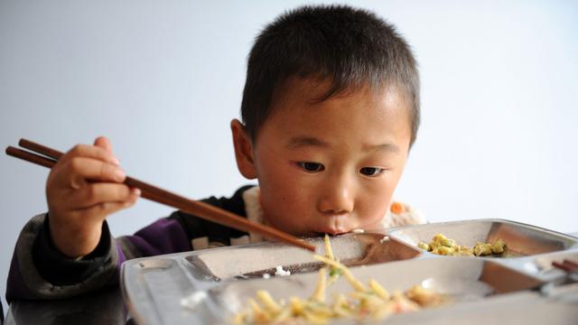 Ein chinesischer Grundschüler isst sein Schulessen mit hölzernen Stäbchen.