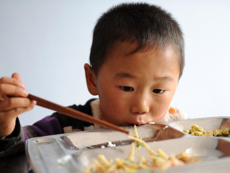 Ein chinesischer Grundschüler isst sein Schulessen mit hölzernen Stäbchen.