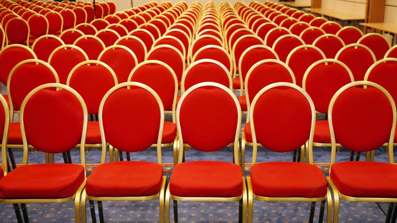 Rote Stühlen stehen in Reihen in einem leeren Saal. Rote Stühlen stehen in Reihen in einem leeren Saal.