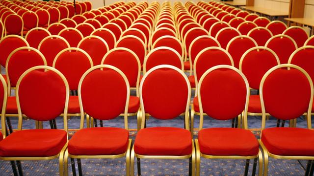 Rote Stühlen stehen in Reihen in einem leeren Saal.