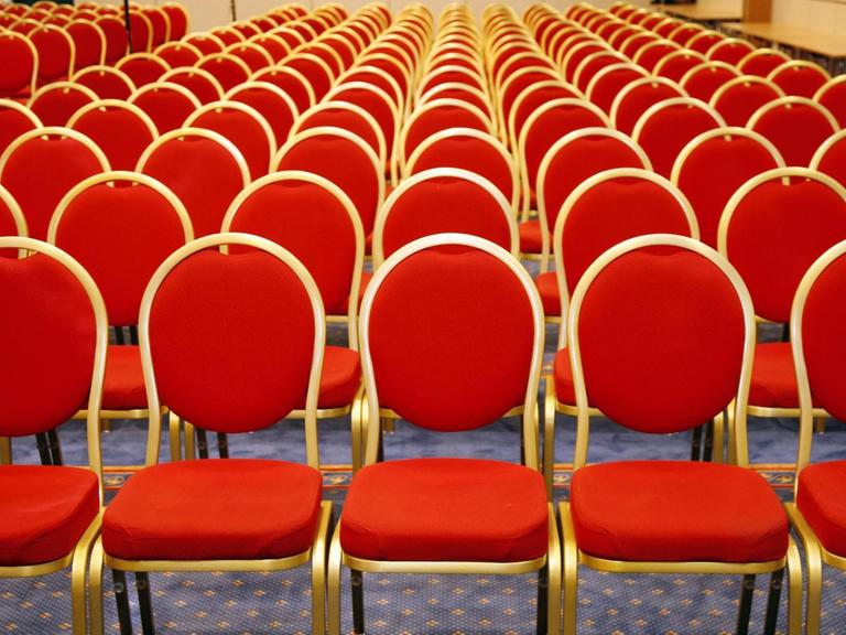 Rote Stühlen stehen in Reihen in einem leeren Saal.
