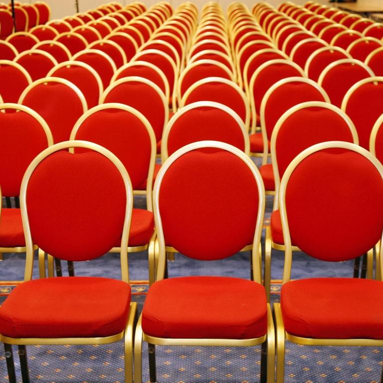 Rote Stühlen stehen in Reihen in einem leeren Saal.