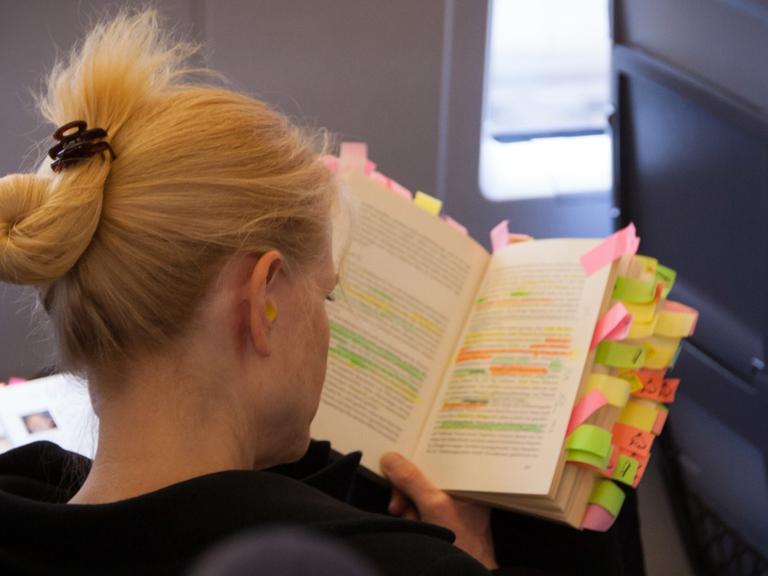 Eine Frau studiert im Zug ein Buch, das mit vielen Markierungen versehen ist.