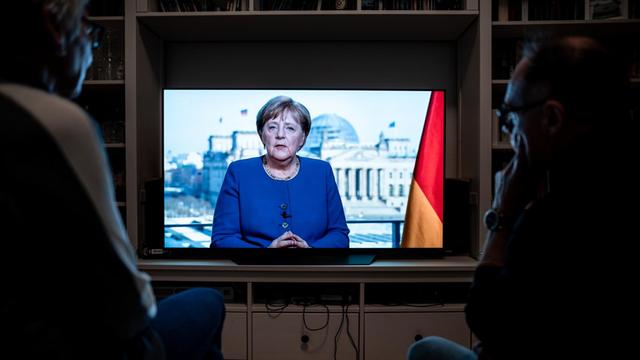 Menschen schauen die Rede der Bundeskanzlerin Angela Merkel (CDU) in einem Wohnzimmer in Oberhausen. Die Bundeskanzlerin redet über die Coronavirus-Pandemie.