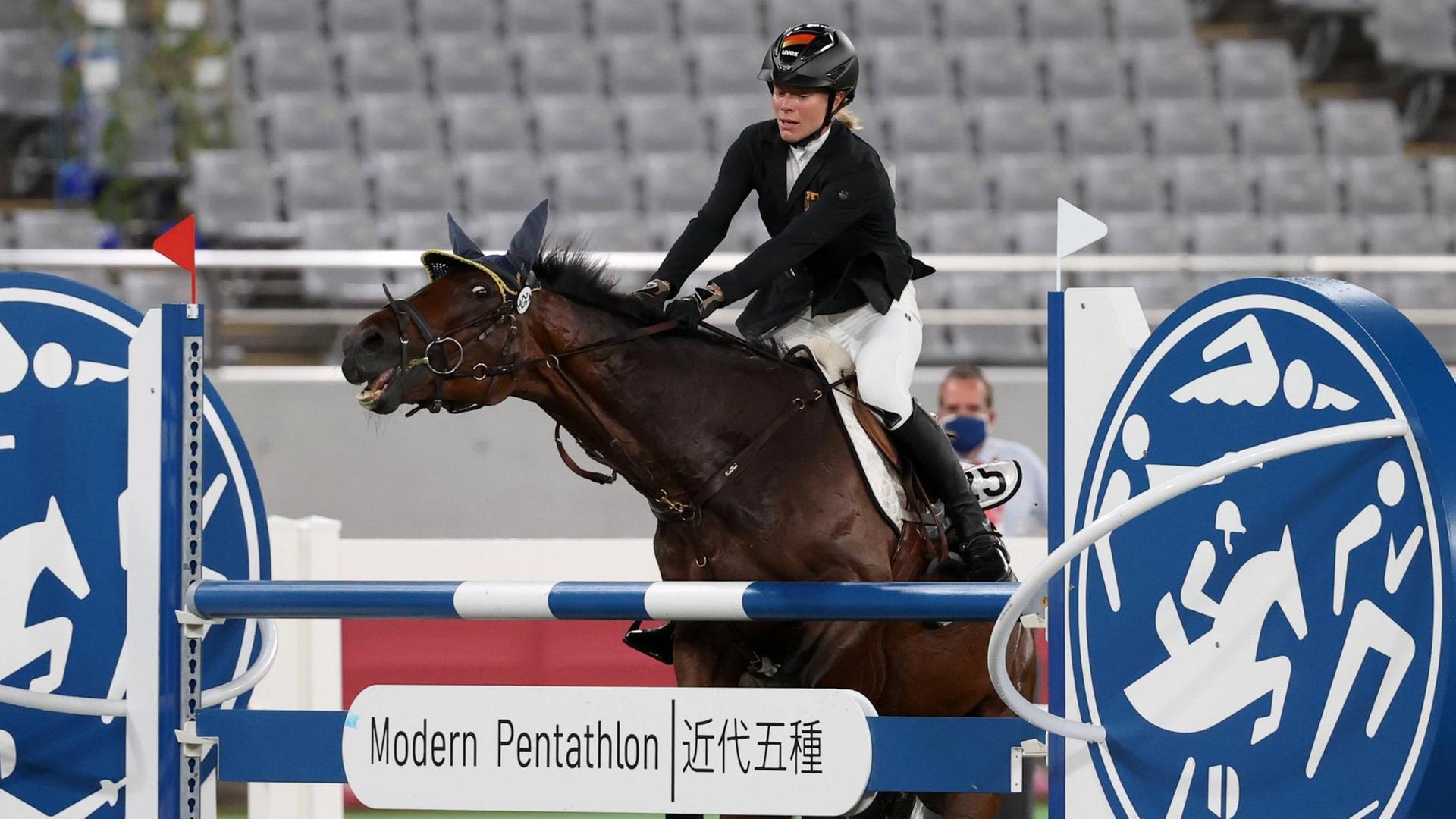 Das Bild zeigt die Reiterin Annika Schleu. Sie sitzt auf einem Pferd. Das Pferd will nicht über ein Hindernis springen. Das war bei den Olmpischen Spielen. Das Bild zeigt die Reiterin Annika Schleu. Sie sitzt auf einem Pferd. Das Pferd will nicht über ein Hindernis springen. Das war bei den Olmpischen Spielen.