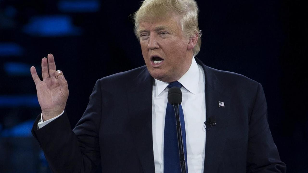 Trump spricht und gestikuliert vor einem dunklen Hintergrund. Trump spricht und gestikuliert vor einem dunklen Hintergrund.