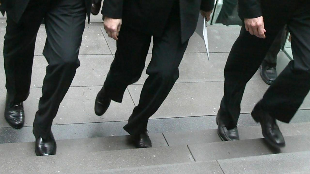 Archivbild: Blick auf die Beine von Edmund Stoiber, Angela Merkel und Guido Westerwelle, die alle in schwarzen Hosen stecken und im Gleichschritt eine Treppe hochgehen.