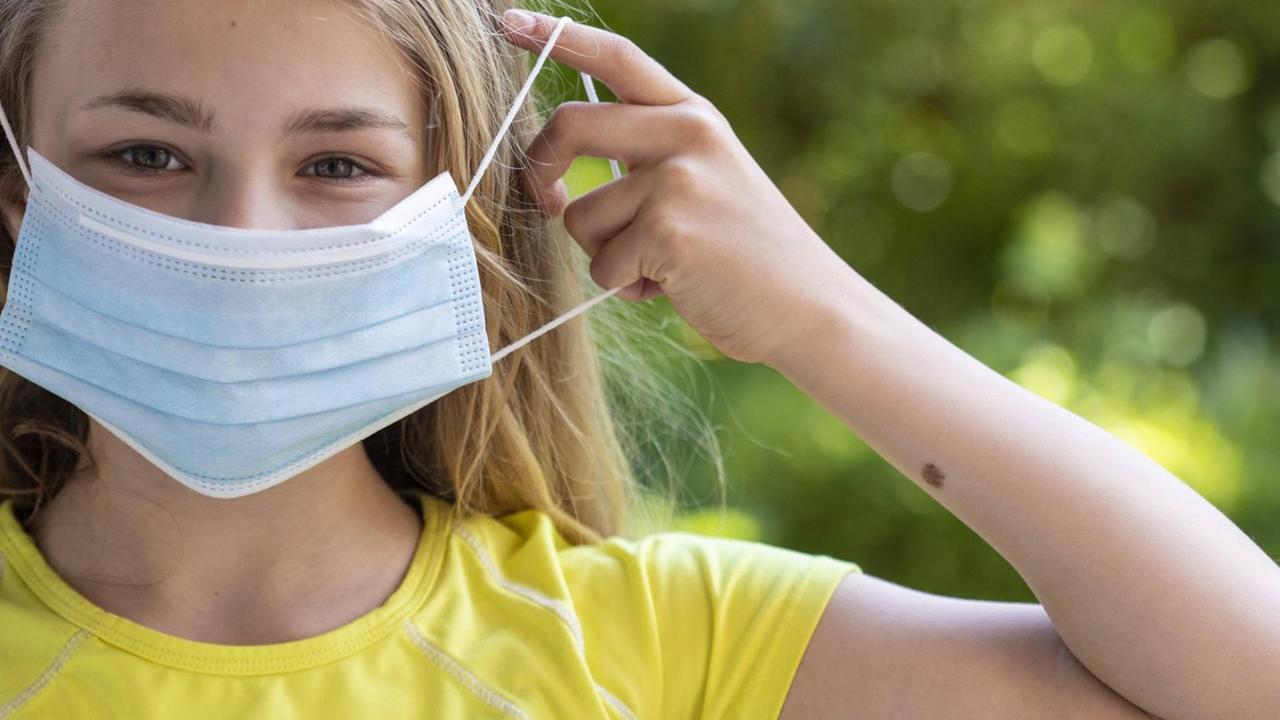 Mädchen in gelbem T-Shirt mit Mund-Nasen-Schutz und auf dem Arm ein Muttermal Mädchen in gelbem T-Shirt mit Mund-Nasen-Schutz und auf dem Arm ein Muttermal