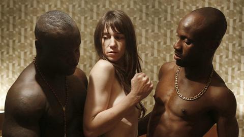 Schauspielerin Charlotte Gainsbourg (M.) im Film "Nymphomaniac" von Lars von Trier. Rechts und links von ihr stehen muskulöse Männer mit nacktem Oberkörper.