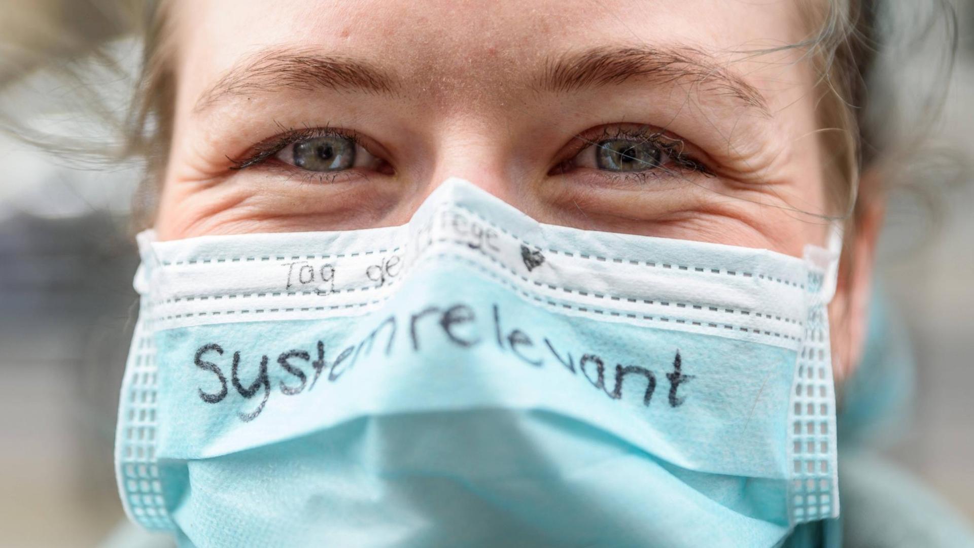 Eine Pflegerin hat das Wort "systemrelevant" auf ihren Mundschutz geschrieben. Eine Pflegerin hat das Wort "systemrelevant" auf ihren Mundschutz geschrieben.