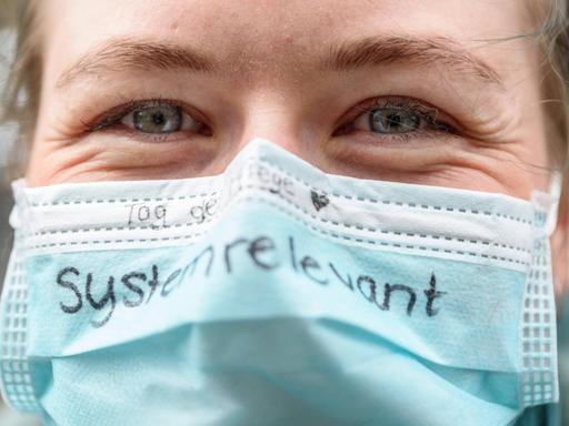 Eine Pflegerin hat das Wort "systemrelevant" auf ihren Mundschutz geschrieben.