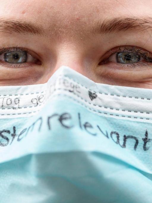 Eine Pflegerin hat das Wort "systemrelevant" auf ihren Mundschutz geschrieben.