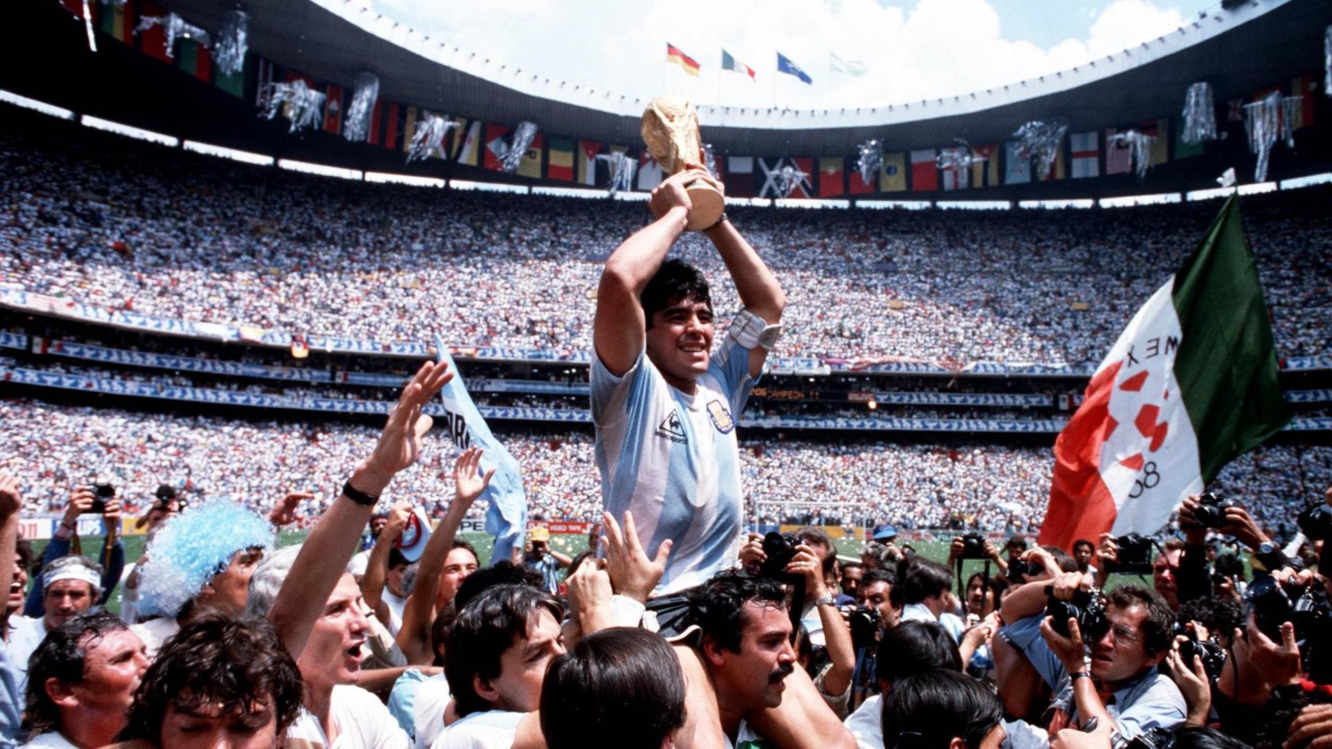 Diego Maradona wird auf den Schultern getragen und hält jubelnd den Weltmeisterpokal 1986 in der Mitte des Stadions hoch. Diego Maradona wird auf den Schultern getragen und hält jubelnd den Weltmeisterpokal 1986 in der Mitte des Stadions hoch.