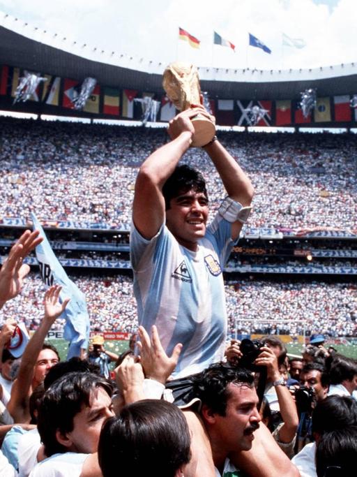 Diego Maradona wird auf den Schultern getragen und hält jubelnd den Weltmeisterpokal 1986 in der Mitte des Stadions hoch.