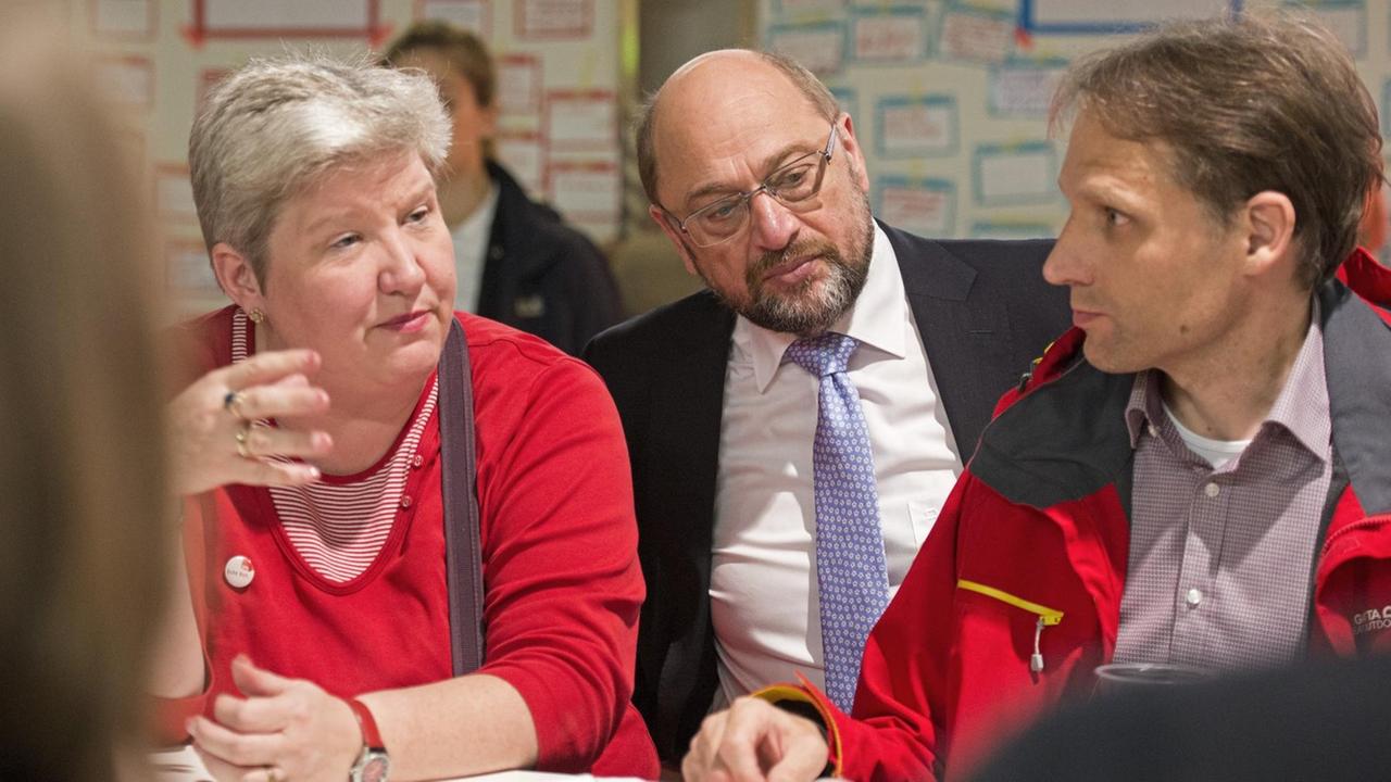 Schulz sitzt in einem Raum hinter einem Mann und einer Frau. Die Frau redet, der Mann und Schulz hören zu. Dahinter unscharf zwei Stellwände mit Organisations-Diagrammen. Schulz sitzt in einem Raum hinter einem Mann und einer Frau. Die Frau redet, der Mann und Schulz hören zu. Dahinter unscharf zwei Stellwände mit Organisations-Diagrammen.