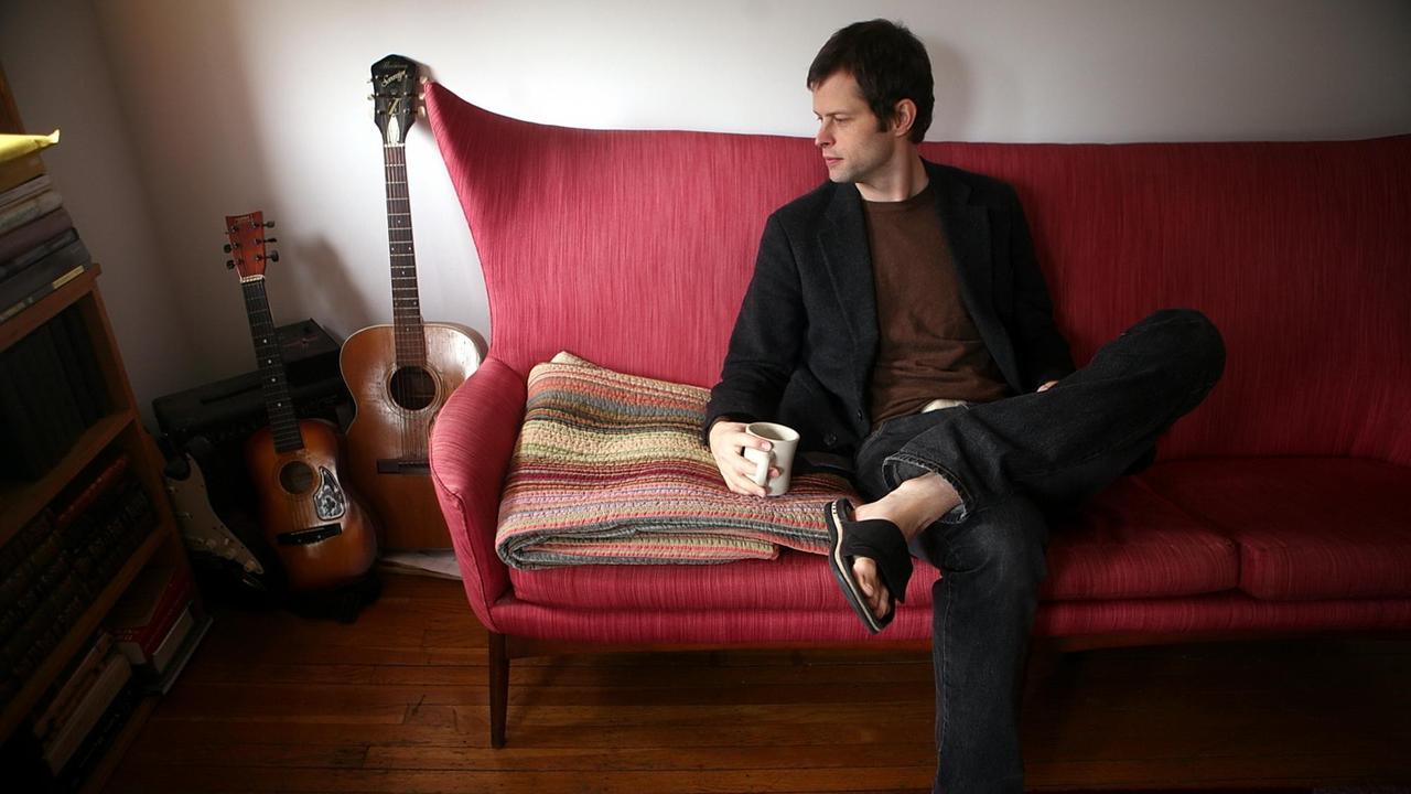 Schriftsteller John Wray sitz in seiner Wohnung in Brooklyn, New York, auf dem Sofa.