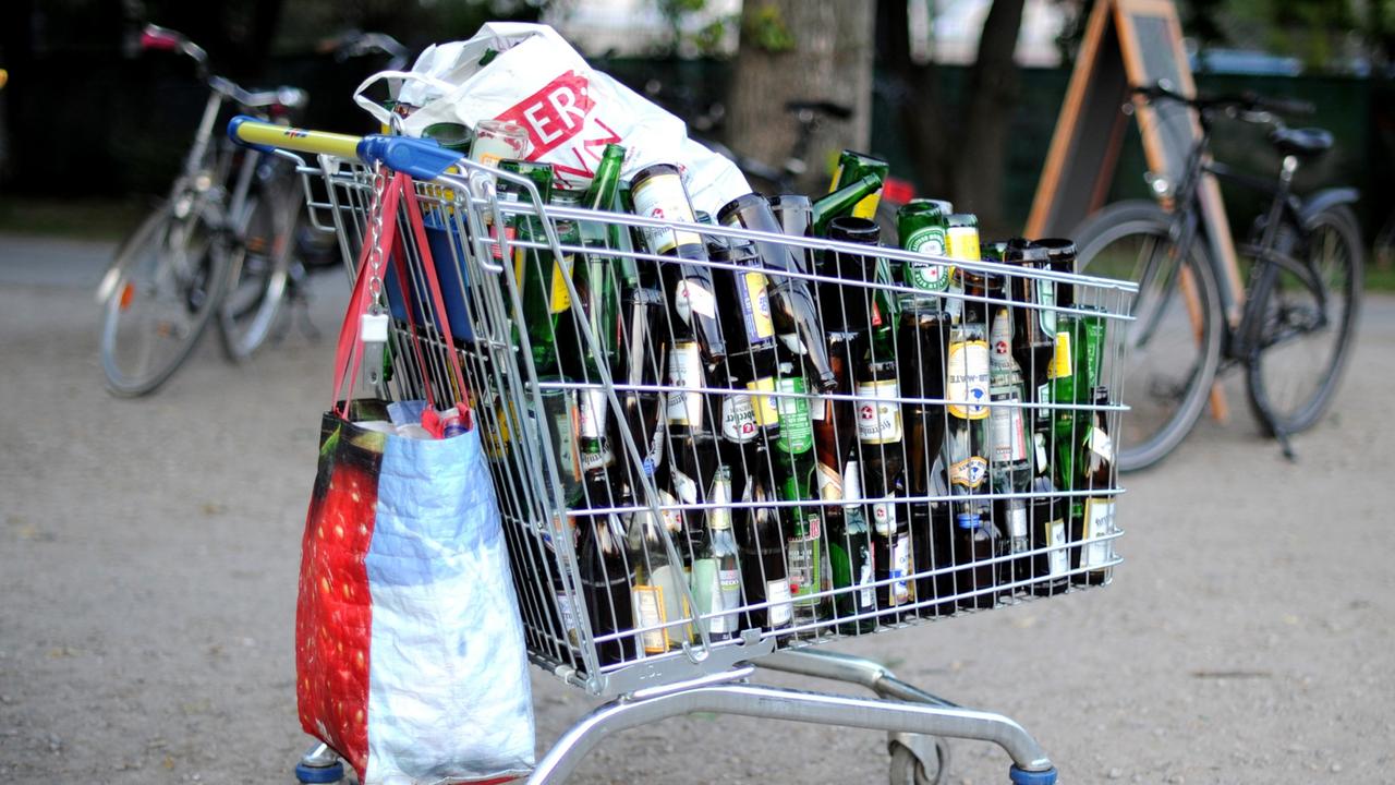 Ein Einkaufswagen mit leeren Bierflaschen steht an einer Wiese in Hannover.