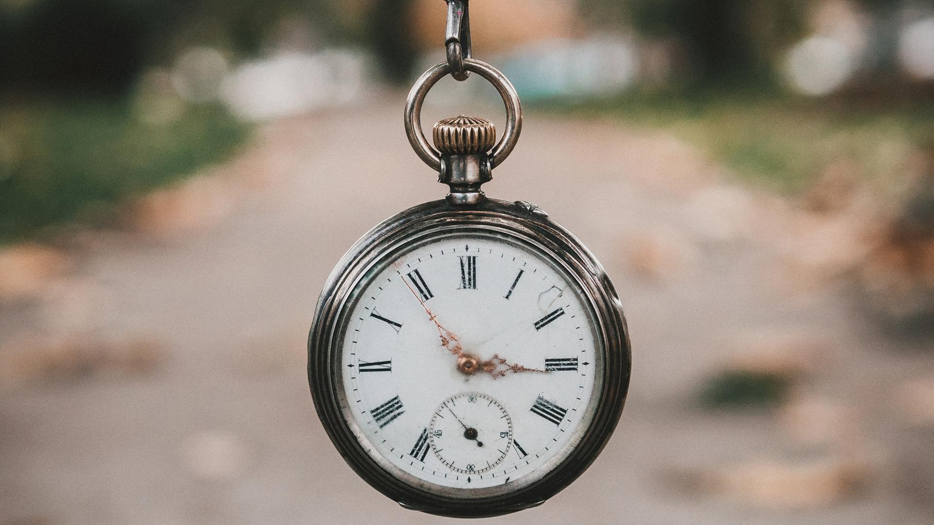 Eine alte Taschenuhr wird an einer Kette vor die Kamera gehalten. Eine alte Taschenuhr wird an einer Kette vor die Kamera gehalten.