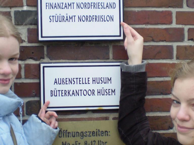 Zwei Friesinnen zeigen stolz das zweisprachige Schild am Finanzamt in Husum