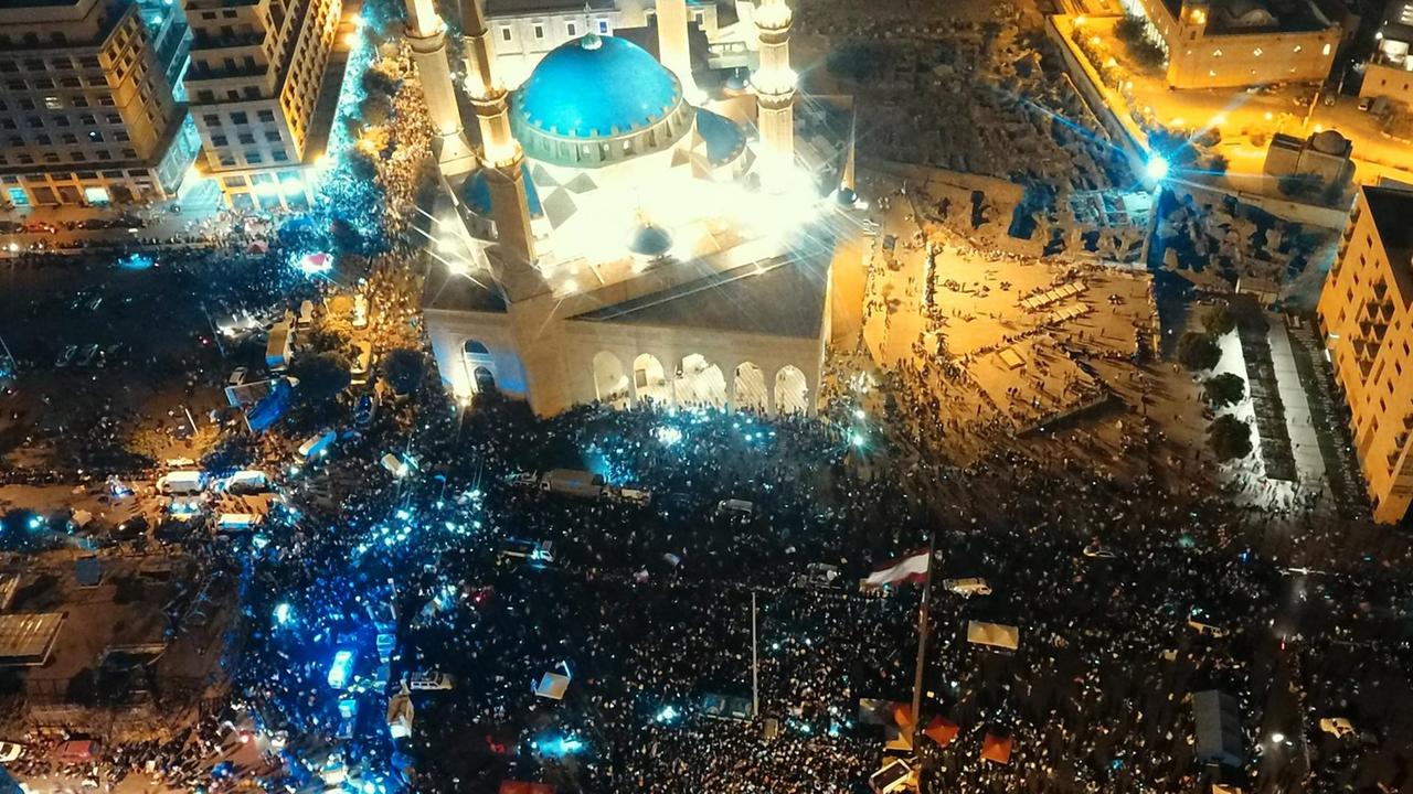 Blick von oben auf Beirut bei Nacht. Tausende Demonstrantinnen und Demonstranten versammeln sich auf zentralen Plätzen. 