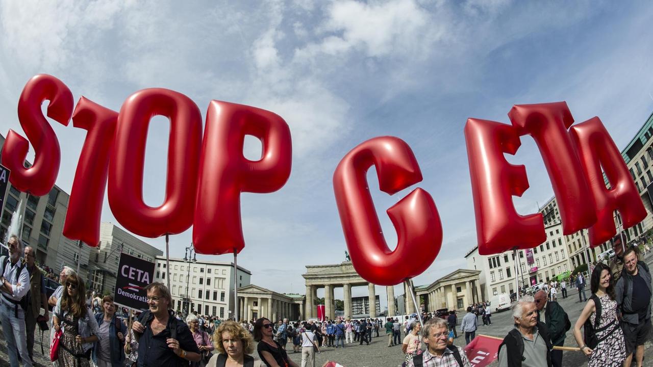 Demonstranten halten rote Buchstaben-Luftballons in den blauen Himme, die die Parole "Stop Ceta" bilden. Im Hintergrund das Brandenburger Tor. Demonstranten halten rote Buchstaben-Luftballons in den blauen Himme, die die Parole "Stop Ceta" bilden. Im Hintergrund das Brandenburger Tor.