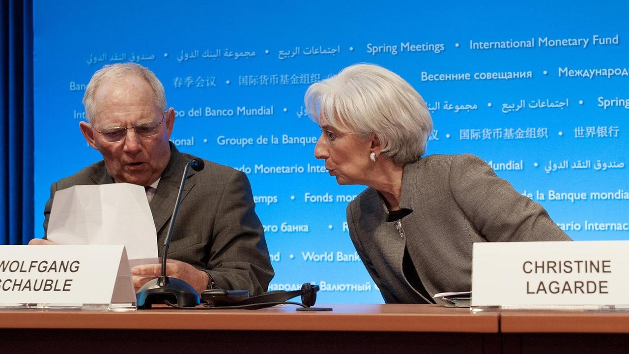 Schäuble und Lagarde reden miteinander auf einem Pressekonferenz-Pult hinter blauem Hintergrund. Schäuble blickt auf ein Dokument.
