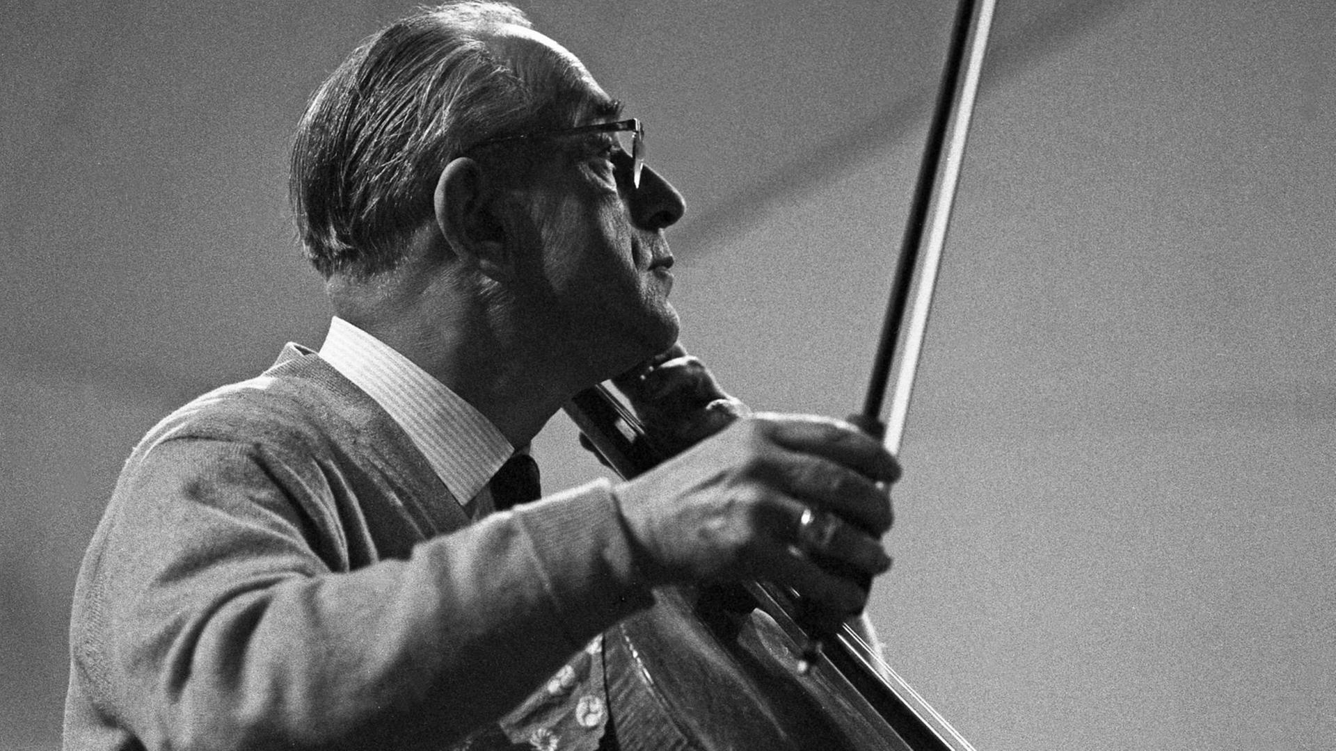 Schwarz-weiß Bild: Ein Mann hält einen Cello-Bogen und schaut nach links, er hat zurückgekämmte Haare, trägt Hemd und Sakko und eine Brille. Schwarz-weiß Bild: Ein Mann hält einen Cello-Bogen und schaut nach links, er hat zurückgekämmte Haare, trägt Hemd und Sakko und eine Brille.