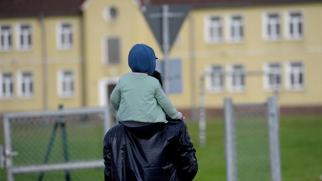 Ein Flüchtling mit einem Kind auf den Schultern geht am 30.10.2015 durch das Flüchtlingscamp Fallingbostel West in Bad Fallingbostel (Niedersachsen).