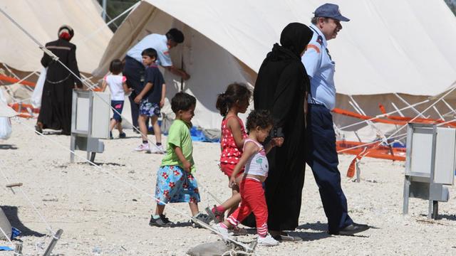 Ein zyprischer Offizier zeigt einer schwarzgekleideten Frau mit drei Kindern in einem Flüchtlingscamp den Weg.