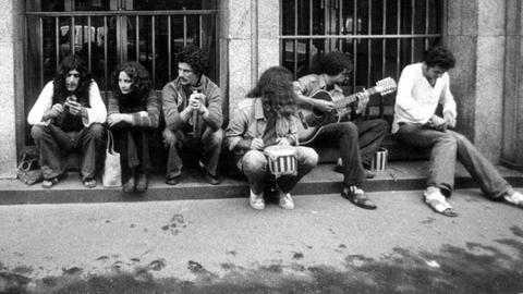 Historische Schwarzweiß-Fotografie von jungen Menschen mit langen Haaren, die auf dem Bordstein sitzen und Musik machen