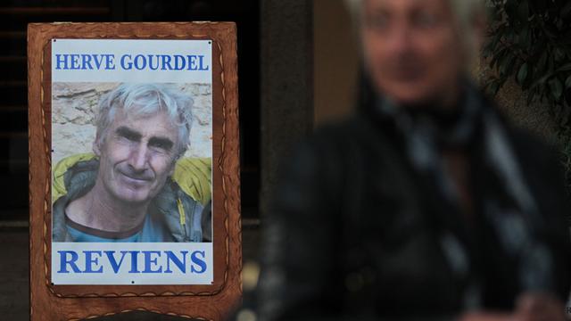 Ein Mann in Algerien steht neben einem Suchplakat, das den entführten französischen Touristen und die Aufschrift "Reviens" (komme zurück) zeigt.