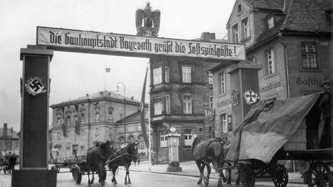 Ein Schild mit der Aufschrift "Die Gauhauptstadt Bayreuth grüßt die Festspielgäste" ist 1944 über einer Straße in Bayreuth an zwei Säulen befestigt. Darüber thront ein Reichsadler.