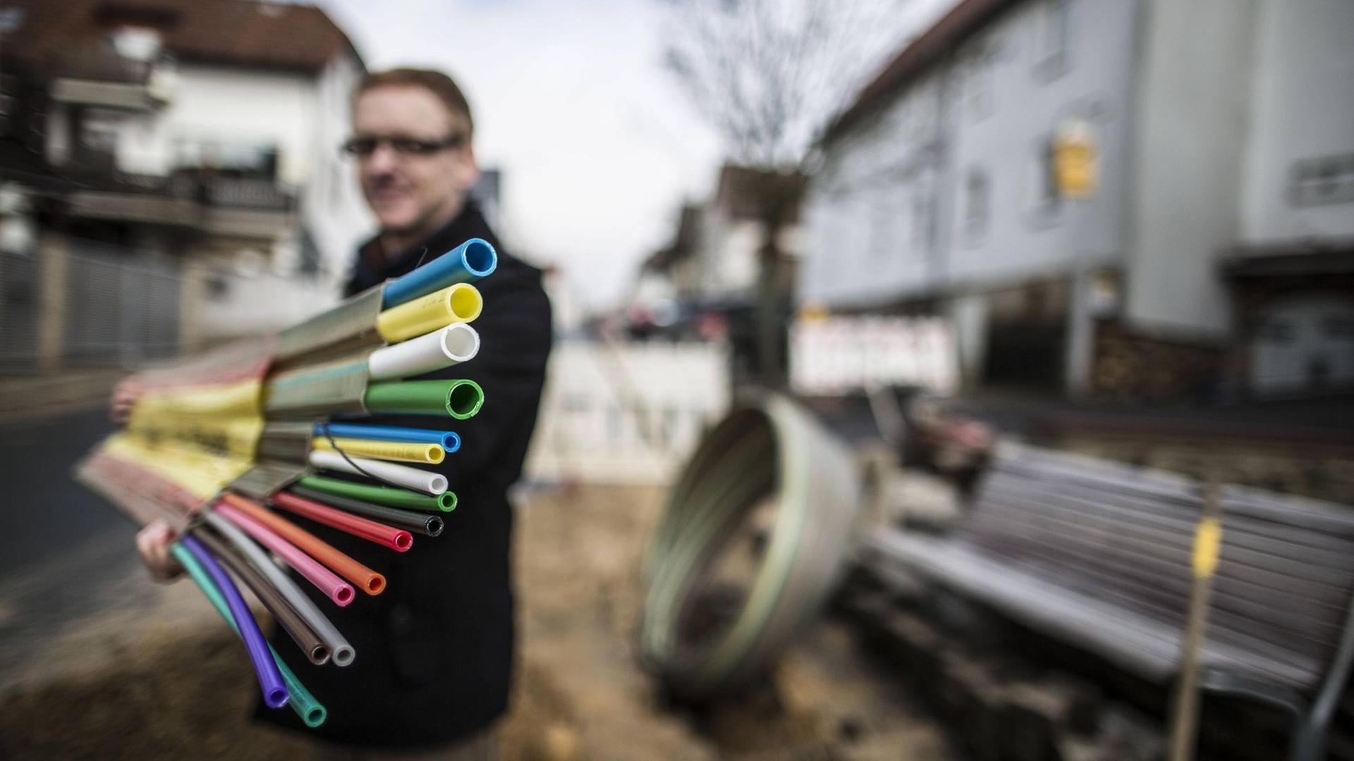 Ein Mann hält vor einer aufgerissenen Straße Leerrohre für den Breitband-Ausbau in die Kamera. Ein Mann hält vor einer aufgerissenen Straße Leerrohre für den Breitband-Ausbau in die Kamera.