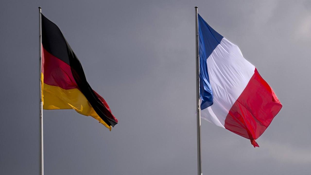 Die deutsche und die französische Flagge wehen vor einem grauen Himmel. Die deutsche und die französische Flagge wehen vor einem grauen Himmel.