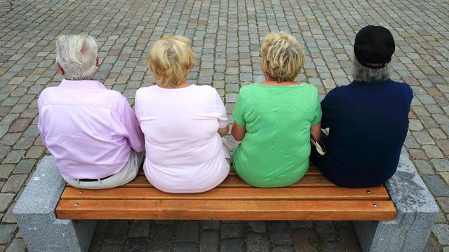 Vier Rentner sitzen mit dem Rücken zum Betrachter auf einer Parkbank.