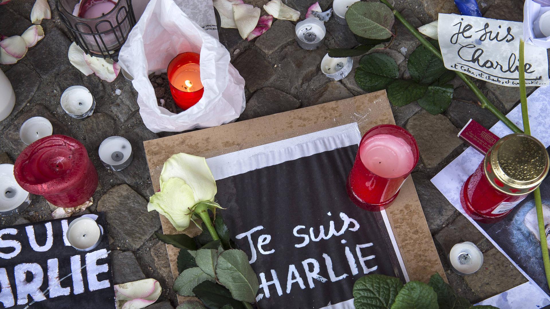 Blumen und Kerzen und Zettel mit der Aufschrift "Je suis Charlie" liegen auf dem Boden.