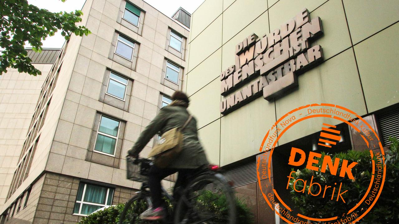 Eine Person fährt auf dem Fahrrad an der Fassade der Staatsanwaltschaft im Justizzentrum Frankfurt mit der Skulptur vorbei. Eine Person fährt auf dem Fahrrad an der Fassade der Staatsanwaltschaft im Justizzentrum Frankfurt mit der Skulptur vorbei.