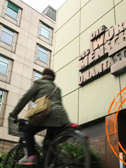 Eine Person fährt auf dem Fahrrad an der Fassade der Staatsanwaltschaft im Justizzentrum Frankfurt mit der Skulptur vorbei.