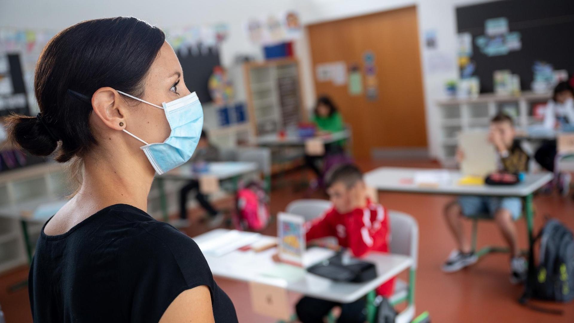Eine Lehrerin mit Mund- und Nasenschutz steht in einer Grundschule. Foto: Sebastian Gollnow/dpa | Verwendung weltweit Eine Lehrerin mit Mund- und Nasenschutz steht in einer Grundschule. Foto: Sebastian Gollnow/dpa | Verwendung weltweit