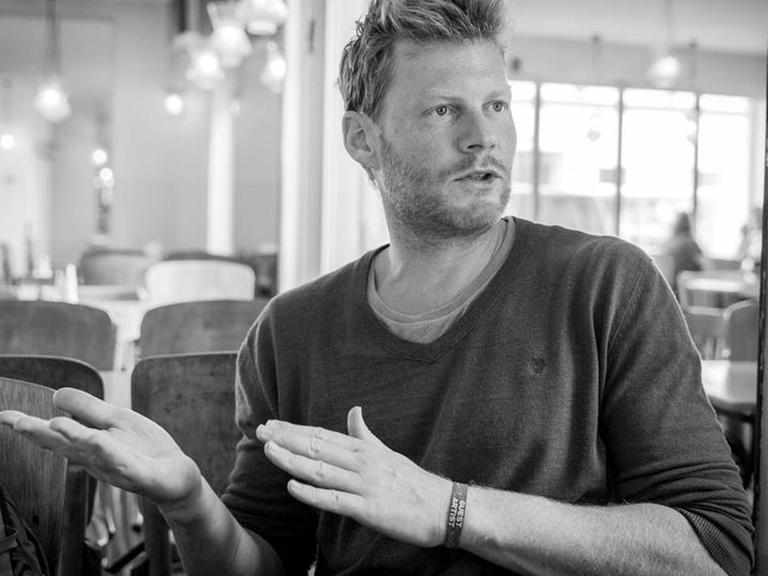 Schwarzweiß-Aufnahme von Christian Felber. Er sitzt gestikulieren und im Gespräch in einem Cafe.