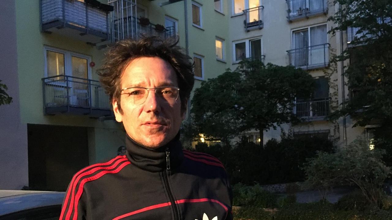 Der Lichtdesigner Georg Veit steht in einem schwarzen Trainingsanzug auf seinem Innenhof in der Münchner Innenstadt. Es ist bereits dunkel, hinter ihm sind Bäume zu sehen und hinter einzelnen Fenstern und Balkonen brennt Licht in den Zimmern. Der Lichtdesigner Georg Veit steht in einem schwarzen Trainingsanzug auf seinem Innenhof in der Münchner Innenstadt. Es ist bereits dunkel, hinter ihm sind Bäume zu sehen und hinter einzelnen Fenstern und Balkonen brennt Licht in den Zimmern.