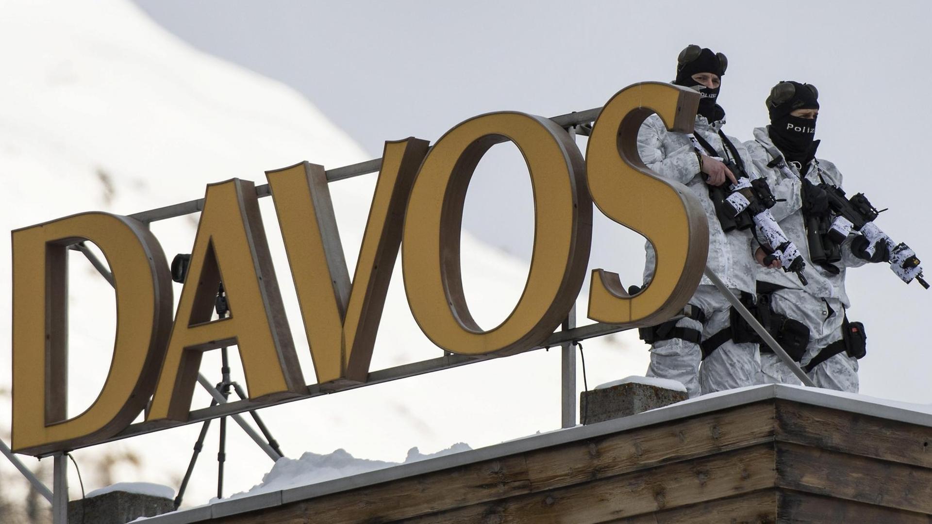 Die beiden Polizisten tragen Maschinengewehre und weiße Tarnkleidung, auf dem Dach steht ein Buchstaben-Neonreklame "Davos". Die beiden Polizisten tragen Maschinengewehre und weiße Tarnkleidung, auf dem Dach steht ein Buchstaben-Neonreklame "Davos".