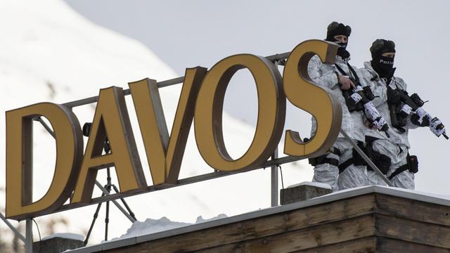 Die beiden Polizisten tragen Maschinengewehre und weiße Tarnkleidung, auf dem Dach steht ein Buchstaben-Neonreklame "Davos".