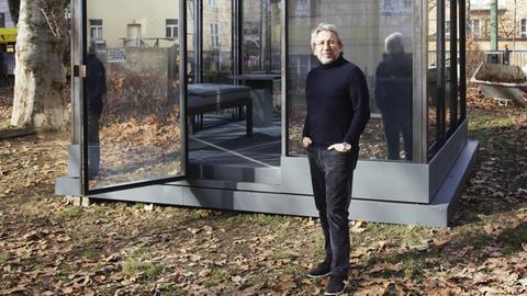 Can Dündar steht von seiner Installation "SİLİVRİ. prison of thought", die aus einer Gefängniszelle im Garten des Gorki Theaters besteht.