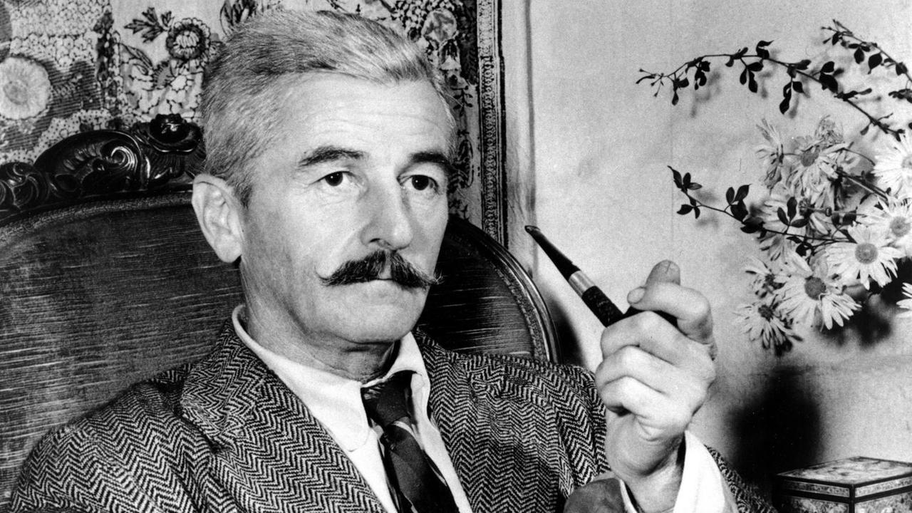 Der US-amerikanische Schriftsteller William Faulkner sitzt mit einer Pfeife in der Hand in einem Sessel Der US-amerikanische Schriftsteller William Faulkner sitzt mit einer Pfeife in der Hand in einem Sessel